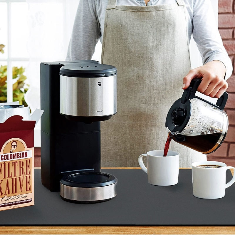 Person pouring coffee into a mug placed on a Super Absorbent Dish Drying Mat. The mat is positioned underneath the mug, with a coffee machine visible in the background - Eagalite